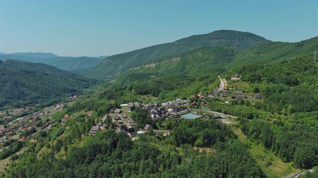 Aerial around view of Drvengrad Kustendorf ethno village on Mokra Gora, Serbia, surrounded by green hills and mountains, 4k