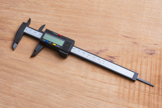 Digital caliper on a wooden surface for technical or industrial design. Precision measuring tool for engineering, machining, quality control, manufacturing, woodworking and workshop applications.