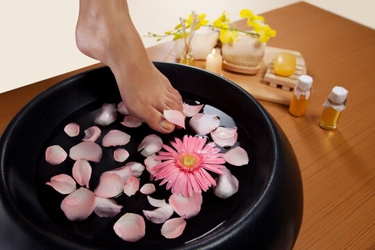 Close-up of a woman's feet and a bowl filled with water and rose petals 