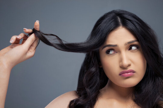 Young woman twisting hair finger over colored background 