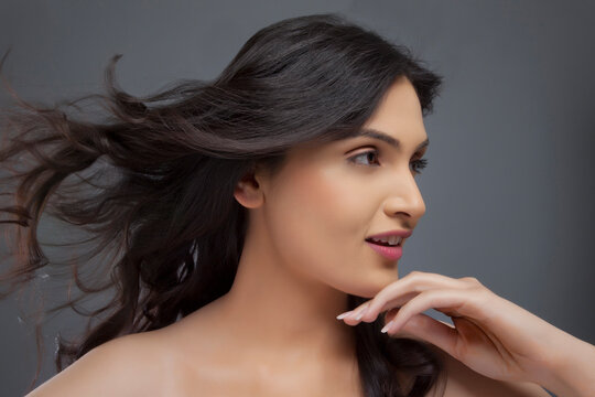 Pretty young female looking away with hair blowing over colored background 
