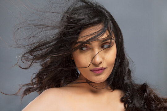 Beautiful young woman with hair blowing over face against colored background 