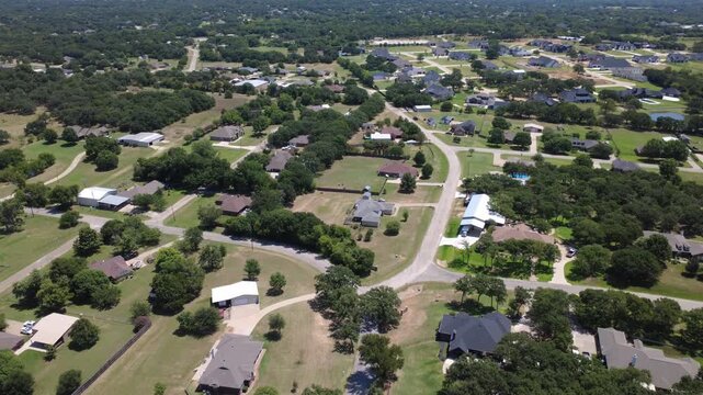 Curving neighborhood streets route local traffic past custom residences along Bethesda Road in Dallas Fort Worth. Elevated viewpoint shows green acreage pastures, wooded backyards. Burleson, TX
