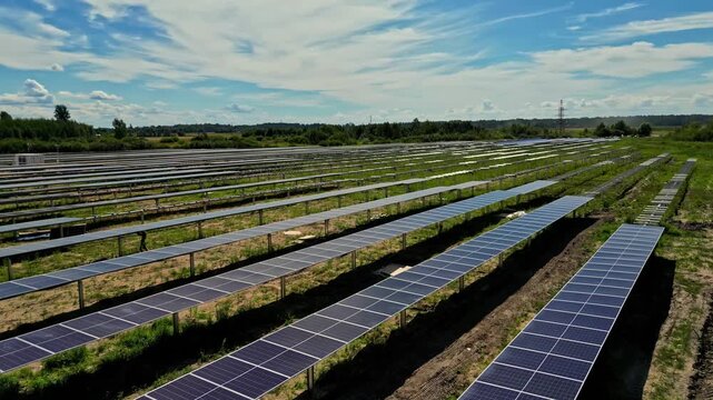 Aerial view of a large solar farm with rows of photovoltaic panels installed in a green field under a blue sky in Latvia.