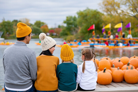 Family with children watching a colorful pumpkin regatta by the lake during an autumn festival with pumpkins, boats and festive fall decorations