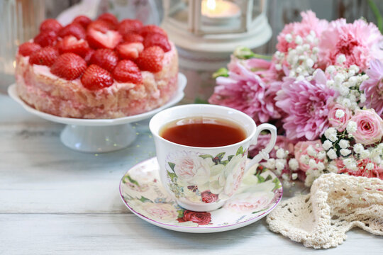Strawberry cake on cake stand, cup of tea and bouquet of flowers.