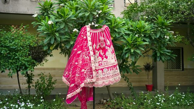 Pink Indian bridal lehenga choli with intricate gold embroidery hanging outdoors