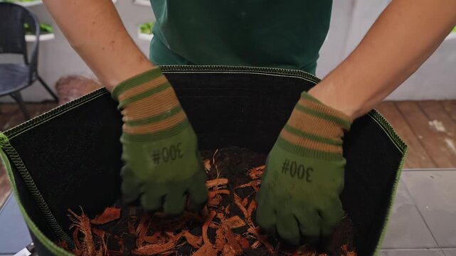 Gloved Hands Mix Bark Mulch and Soil in a Fabric Planter, Demonstrating Sustainable Garden Care From an Elevated Close View