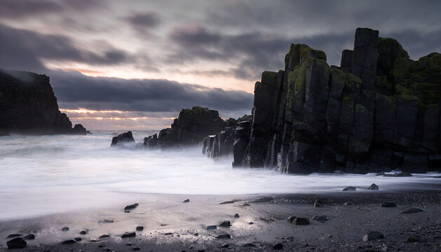 Dramatic rocky beach with dark cliffs at sunset