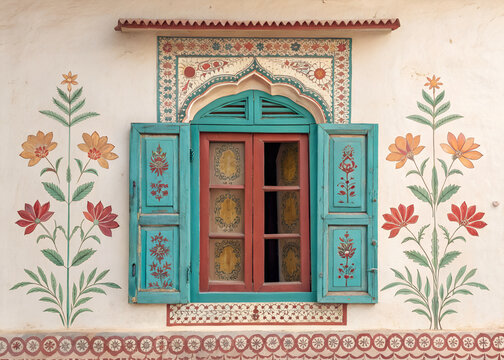 Traditional Indian window with colorful hand-painted floral shutters, carved wooden border, faded turquoise, saffron and crimson colors,