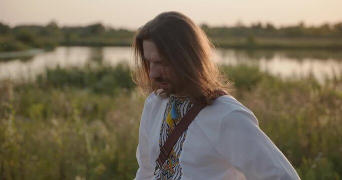 Caucasian man with long hair and Ukrainian traditional folk attire walk wandering on nature. 4K 10-bit