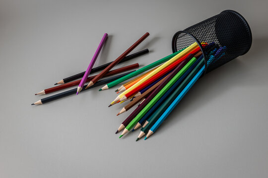 Colored Pencils Spill from Black Mesh Holder on Gray Surface