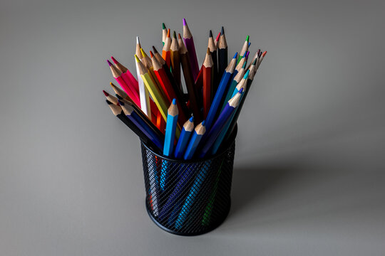 Vibrant Colored Pencils in Black Mesh Holder on Gray Background