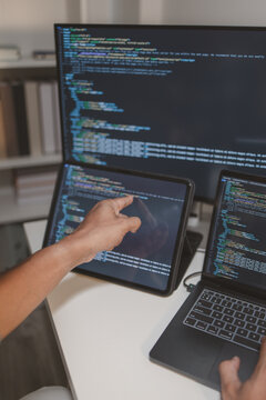 Professional software developer coding across laptop, tablet, and monitor in a modern workspace. Multi-device programming, debugging, software engineering, and application development workflow.