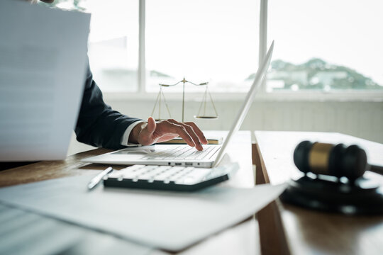 Lawyer working on a laptop at a desk with a gavel, scales of justice, documents and calculator, representing legal services, business law and professional consultation.
