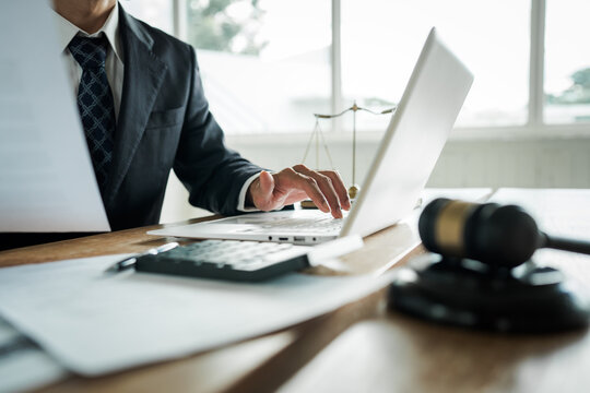 Lawyer working on a laptop at a desk with a gavel, scales of justice, documents and calculator, representing legal services, business law and professional consultation.