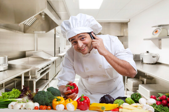 Chef talking on a mobile phone while holding a bell pepper 