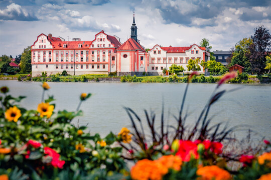 Picturesque summer view of Maria Ward Realschule - beautiful palace on the banks of Inn River with blooming flowers on foreground. Wonderful morning scene of Germany, Europe. 