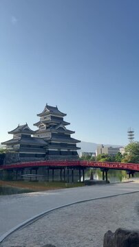 Static vertical portrait nine by sixteen shot of Matsumoto Castle in Nagano Japan showing the bright red Uzumi bridge crossing the water moat under a clear morning sky broll