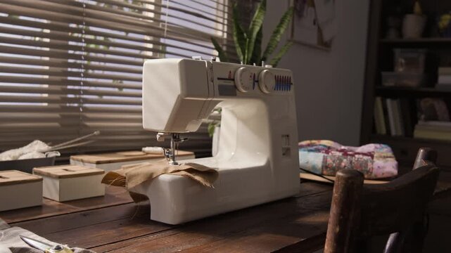 Sewing machine standing on wooden table with fabric under needle in home workshop, low angle view. Footage suitable for DIY craft tutorials, tailoring business promotions, or hobby marketing