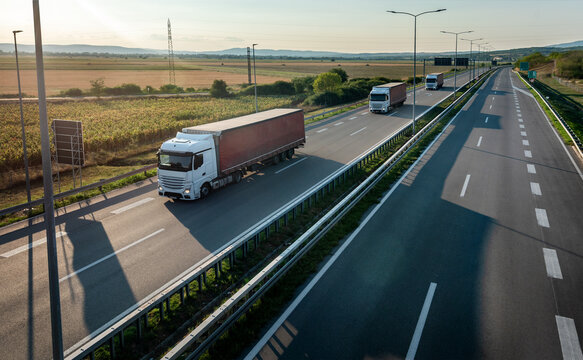 Convoy of three transportation trucks with red containers on highway, cargo transportation concept in springtime - freight service, with a dramatic sunset sky in background