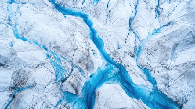 Aerial view of a glacier with vivid turquoise meltwater rivers carving icy white crevasses and flowing through fractured blue glacier ice