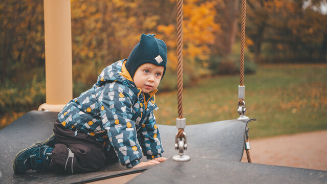 Toddler Boy Crawling on Playground Swing Platform in Autumn Park