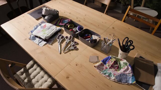 High angle view of wooden table arranged with sewing tools, scissors, threads, and patchwork fabrics. Video is ideal for promoting DIY craft tutorials, quilting workshops, or hobby classes