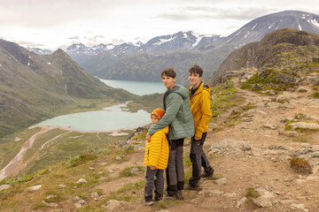Fototapeta premium Beautiful european family with children and pet dog hiking Knutshoe summit with blue lake in mountain landscape in Jotunheimen National Park in Norway, mountains of Besseggen in background, cloudy sky