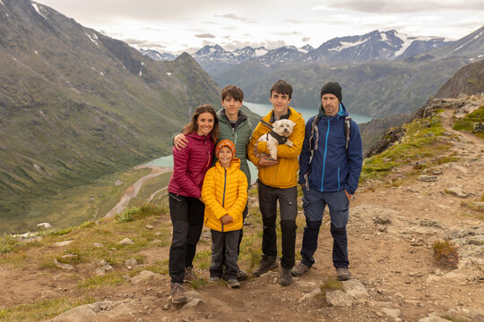 Beautiful european family with children and pet dog hiking Knutshoe summit with blue lake in mountain landscape in Jotunheimen National Park in Norway, mountains of Besseggen in background, cloudy sky