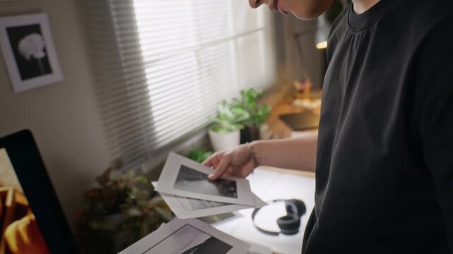 Young Asian male designer holding and reviewing printed black and photographs in creative home office studio. Video is ideal for creative agency promos or photography school ads