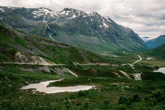Fv63 Trollstigen scenic road winding through a green glacial valley toward high snow-capped mountains in M&oslash;re og Romsdal, Norway.