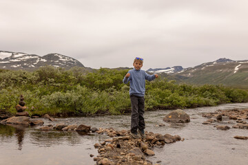 Fototapeta premium Beautiful european family with children and pet dog hiking Knutshoe summit with blue lake in mountain landscape in Jotunheimen National Park in Norway, mountains of Besseggen in background, cloudy sky