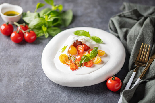 Salad with burrata cheese and tomatoes in a plate on the table. Caprese salad.