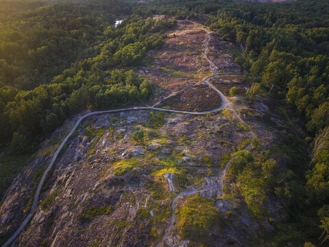 Aerial view of Anggard Mountains with rocky terrain, winding trails, and lush forest during golden hour in Gothenburg, Vastra Gotaland County, Sweden.