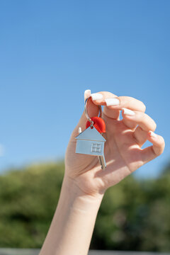 House-shaped keychain and house key held in hand outdoors against blue sky with copy space