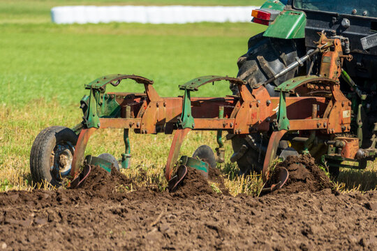 Moldboard plow turning dark soil in a summer agricultural field