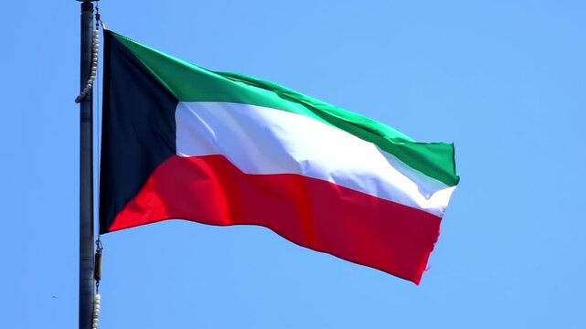 Low angle view of Kuwait national flag waving on flagpole against clear blue sky.