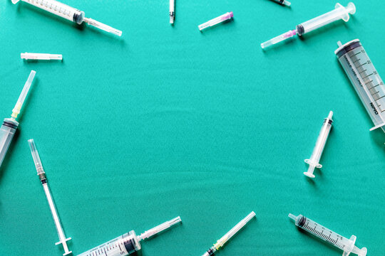 Various syringes scattered on a teal surface, viewed from above.