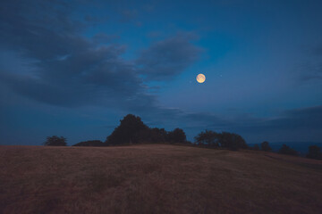 Full Moon, stars and planets above landscape silhouettes in blue hour time. © astrosystem