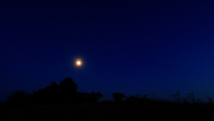 Moon on a twilight sky with stars, planets and landscape mountain silhouettes. © astrosystem