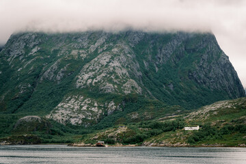 Red wooden rorbu cabin nestled in a rocky coastal cove surrounded by evergreen trees along the Helgelandskysten ferry route in Nordland, Norway © Michele