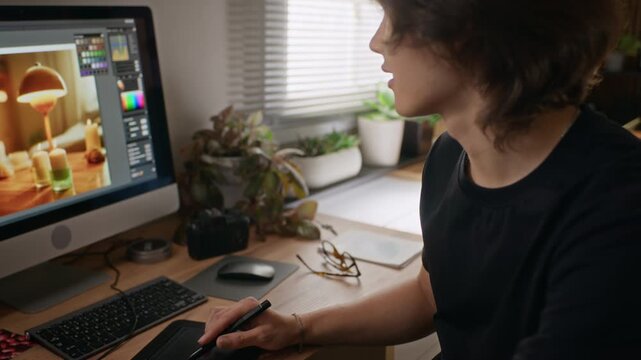 Young Asian male designer using stylus and graphics tablet to edit photos on computer. Footage is ideal for promoting remote work, digital art software, and creative freelance careers