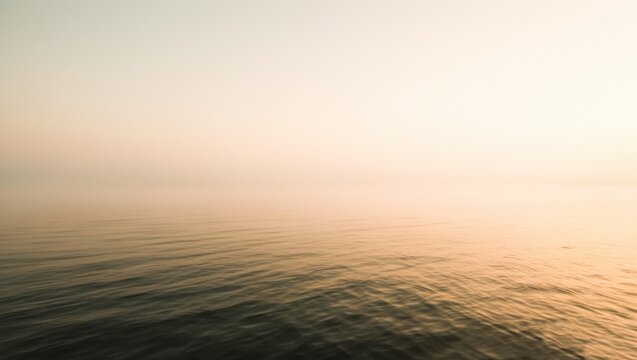 Minimalist horizon of calm water blending into warm misty sky