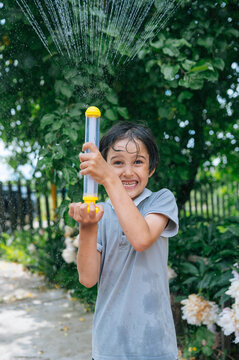 A smiling boy sprays water with a toy in the garden