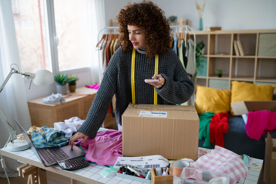 Entrepreneur processing ecommerce clothing order with smartphone and package