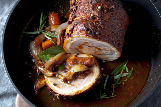 A dark pan contains rolled roast pork and braised vegetable