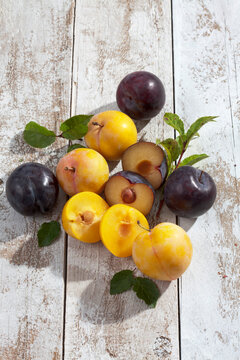 Sliced and whole yellow and black gages (Prunus domestica subsp. italica) on white wooden table, studio shot