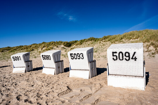 Four white beach chairs stand on the sandy beach of Sylt