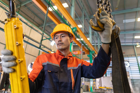 Asian engineer operating hoist crane in industrial factory. Focused professional worker handling heavy equipment with precision.